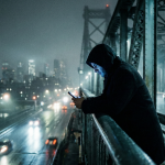 Eine Person steht nachts auf einer Brücke, beleuchtet durch ein Smartphone. Symbolbild für digitale Manipulation in Volker Gerlings 'Der Seelsorger'.